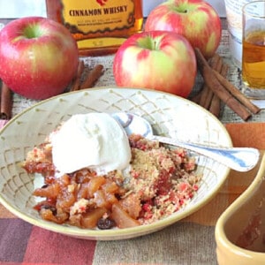 A bowlful of Fireball Apple Crisp topped with ice cream with whole apples in the background.