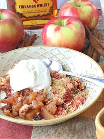 A bowlful of Fireball Apple Crisp topped with ice cream with whole apples in the background.