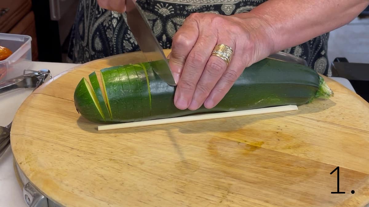 A pair of hands slicing a zucchini to make a Hasselback Zucchini.