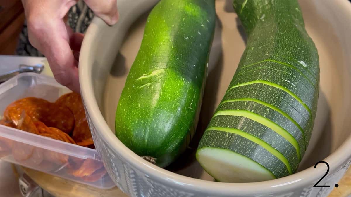 Two Hasselback sliced zucchini in a tan oval baking dish.