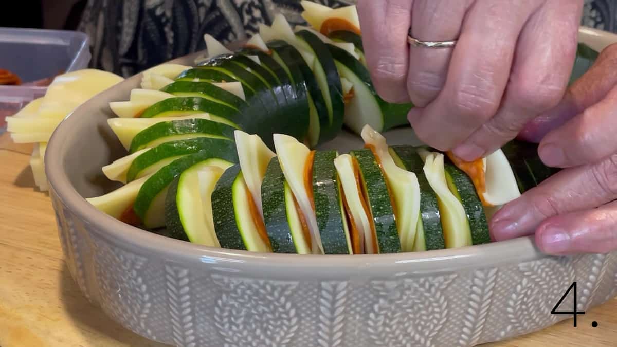 A tan oval baking dish filled with Pepperoni Pizza Hasselback Zucchini before baking.