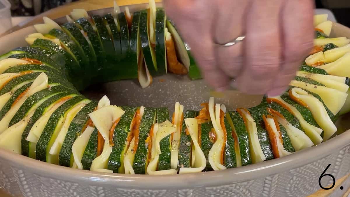 Salt and pepper being added to a Hasselback Zucchini with cheese and pepperoni before baking.