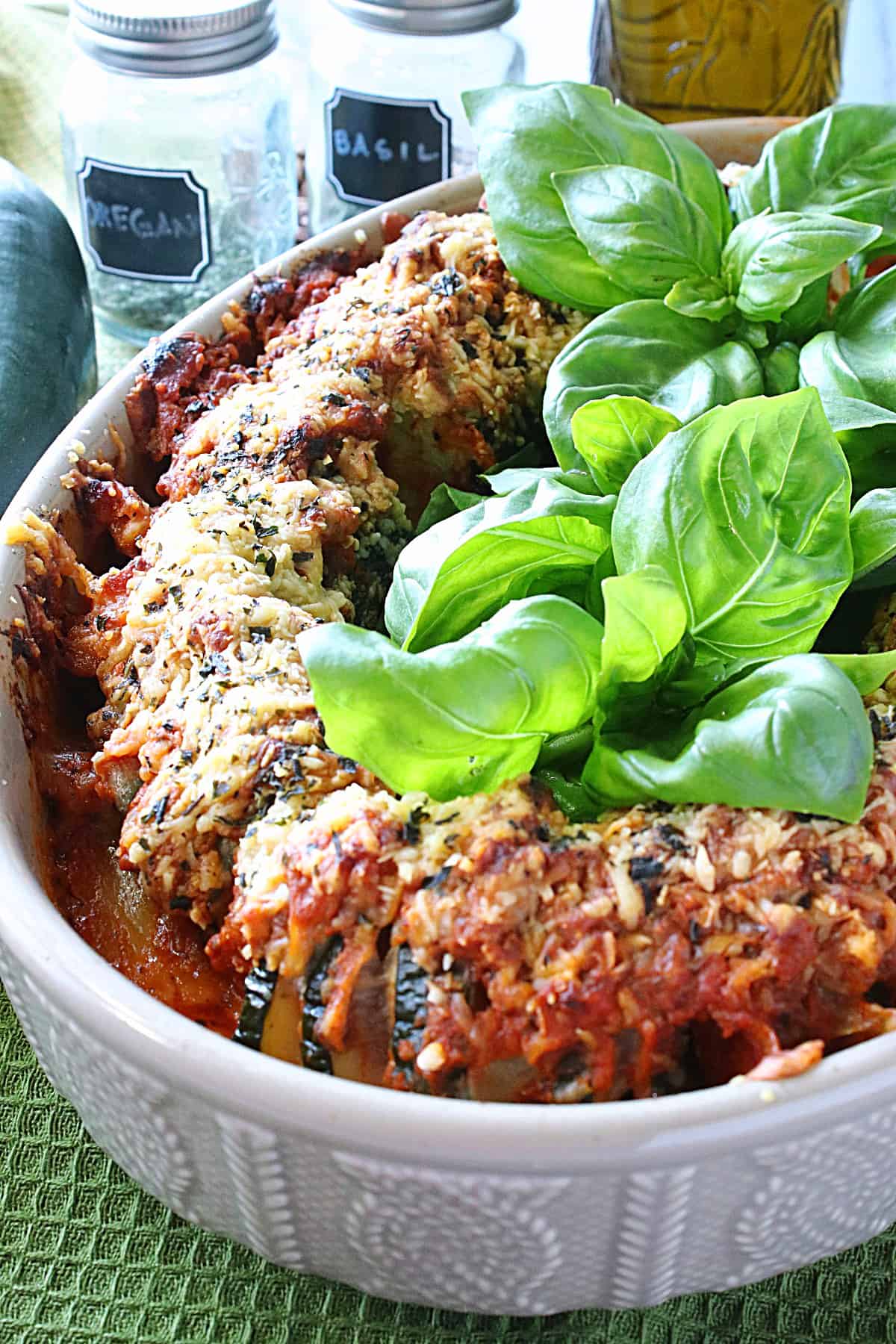 Two Pepperoni Pizza Hasselback Zucchini in an tan oval baking dish with fresh basil in the center.