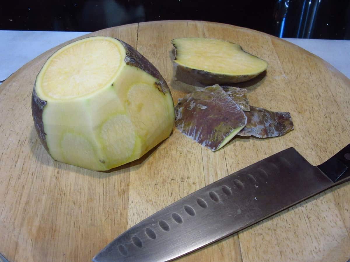 A rutabaga on a cutting board with some of the skin taken off.