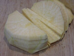 A rutabaga on a cutting board being sliced into fry shapes.