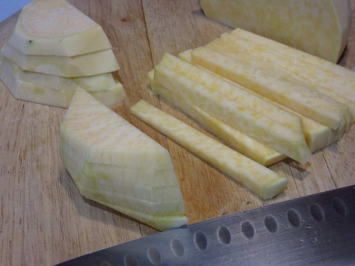 A rutabaga being sliced into French fry shapes on a wooden cutting board.