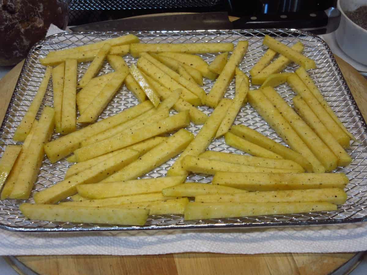 An air fryer tray covered with seasoned Rutabaga Fries before cooking.