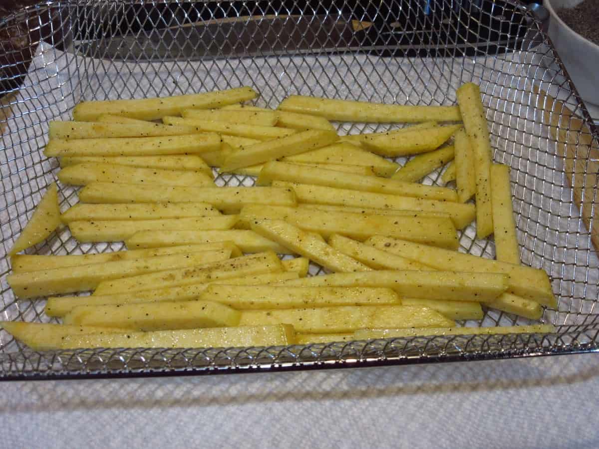 An air fryer tray lined with seasoned Rutabaga Fries before cooking.