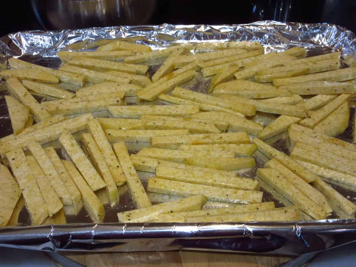 A baking sheet lined with foil and covered with seasoned Rutabaga Fries before cooking.