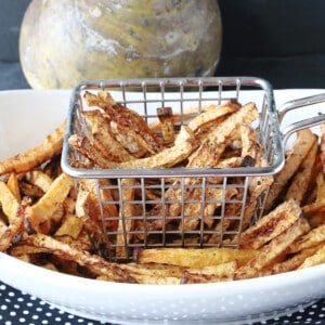 A oval white bowl along with a fry basket filled with golden brown Rutabaga Fries.