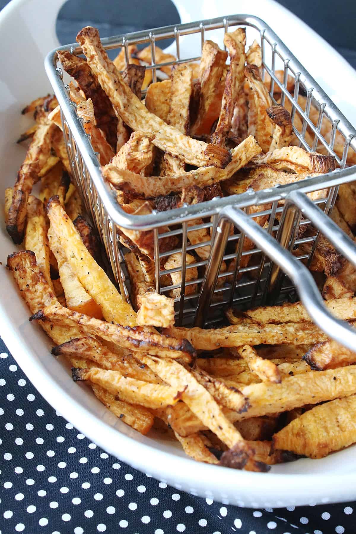 A wire basket and a white bowl filled with rutabaga fries.