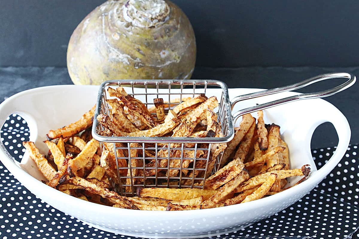 An oval white bowl with a fry basket inside all filled with cooked rutabaga fries.