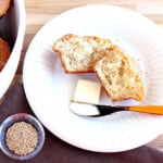 A Sesame Seed Dinner Roll on a white plate with a pat of butter and a knife.