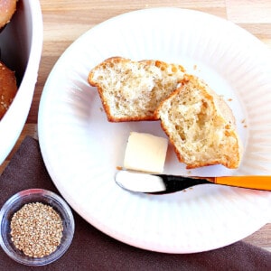 A Sesame Seed Dinner Roll on a white plate with a pat of butter and a knife.