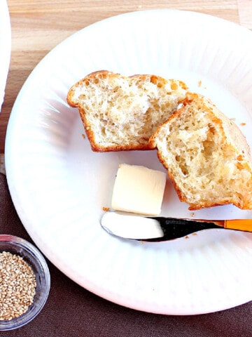 A Sesame Seed Dinner Roll on a white plate with a pat of butter and a knife.