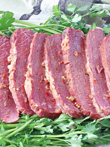 Slices of Slow Cooker Corned Beef on a platter surrounded by fresh parsley.