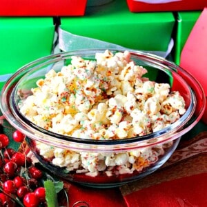 A glass bowl filled with White Chocolate Popcorn with red and green sugar for Christmas.