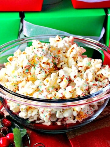 A glass bowl filled with White Chocolate Popcorn with red and green sugar for Christmas.