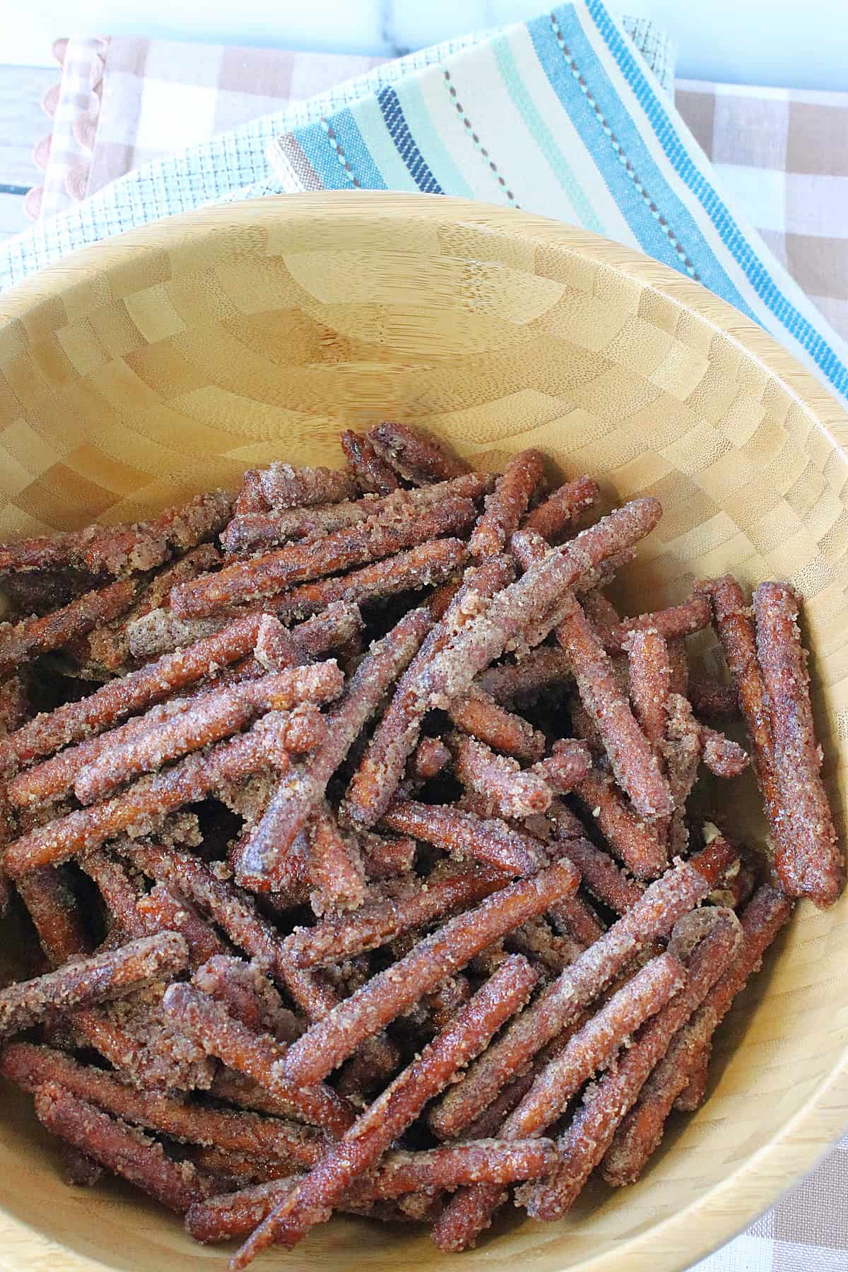 A wooden bowl filled with Cinnamon Sugar Pretzel Sticks with blue napkins underneath.