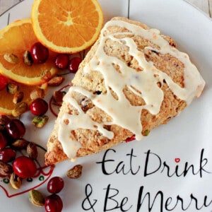 A Cranberry Orange Scone on a holiday plate along with cranberries and pistachios.