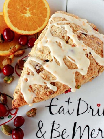 A Cranberry Orange Scone on a holiday plate along with cranberries and pistachios.