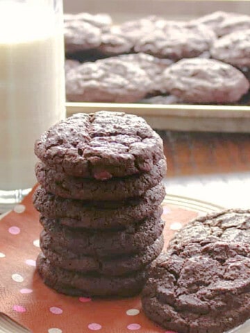 A tall stack of Double Chocolate Malted Cookies with a glass of milk in the background.