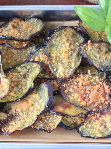 A bunch of Eggplant Chips on a baking sheet covered with grated Parmesan cheese.