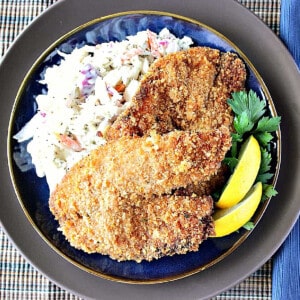 Homemade Fried Tilapia on a blue plate along with coleslaw and lemon wedges.