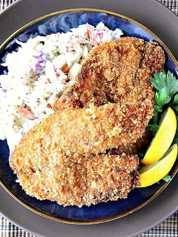 Homemade Fried Tilapia on a blue plate along with coleslaw and lemon wedges.