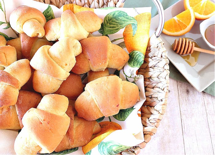 A bunch of Honey Orange Crescent Rolls in a basket with a pretty napkin.