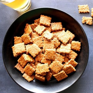 A black bowl filled with square Honey Sesame Seed Crackers.