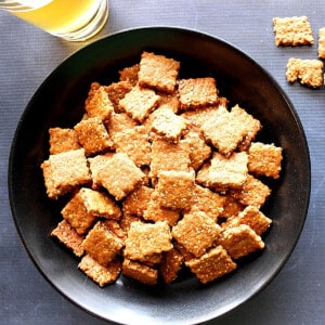 A black bowl filled with square Honey Sesame Seed Crackers.