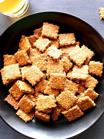 A black bowl filled with square Honey Sesame Seed Crackers.