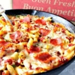A cast iron skillet filled with Pepperoni Pizza Mac and Cheese with a pizza box in the background.