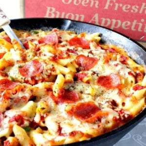 A cast iron skillet filled with Pepperoni Pizza Mac and Cheese with a pizza box in the background.