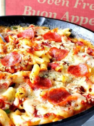 A cast iron skillet filled with Pepperoni Pizza Mac and Cheese with a pizza box in the background.