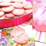 Two Pink Lemonade Cookies on a napkin with a glass of pink lemonade next to them.