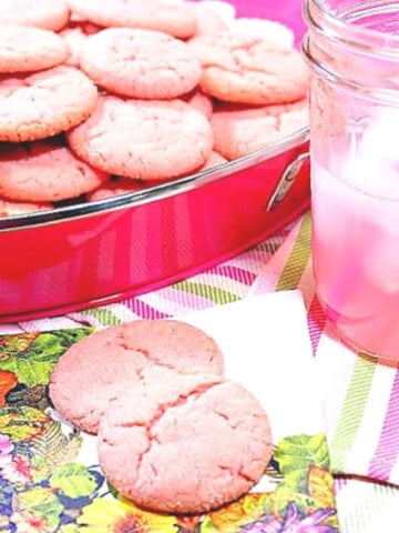 Two Pink Lemonade Cookies on a napkin with a glass of pink lemonade next to them.