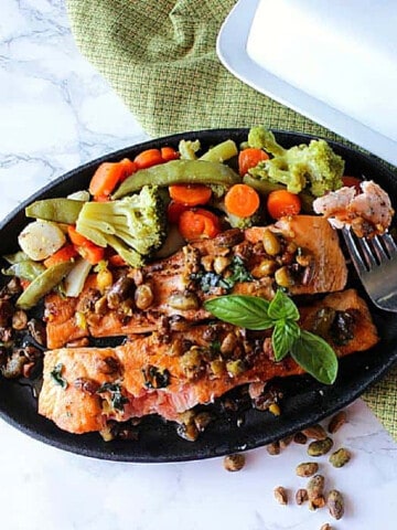 Two Salmon Fillets with Pistachio Basil Butter in a cast iron skillet topped with pistachios.