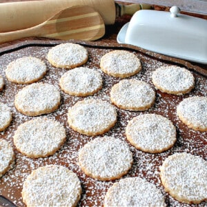 A wooden tray filled with Toasted Coconut Shortbread Cookies with a confectioners sugar dusting.