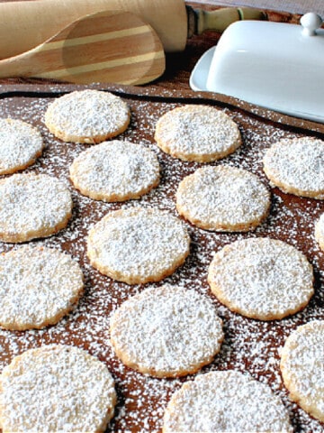 A wooden tray filled with Toasted Coconut Shortbread Cookies with a confectioners sugar dusting.