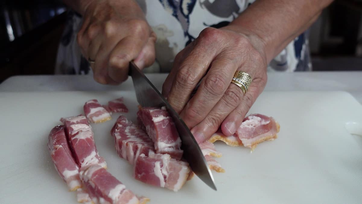 Hands and a knife cutting bacon.