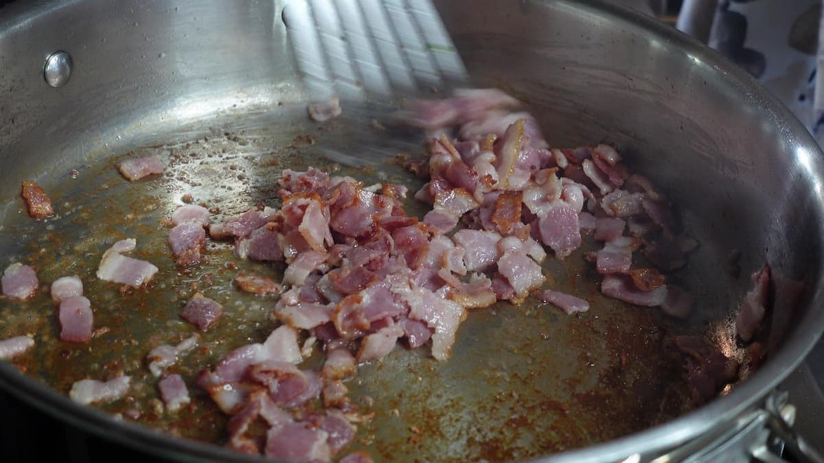 Frying cut up bacon in a skillet to make Bacon Bourbon Green Beans Almondine.
