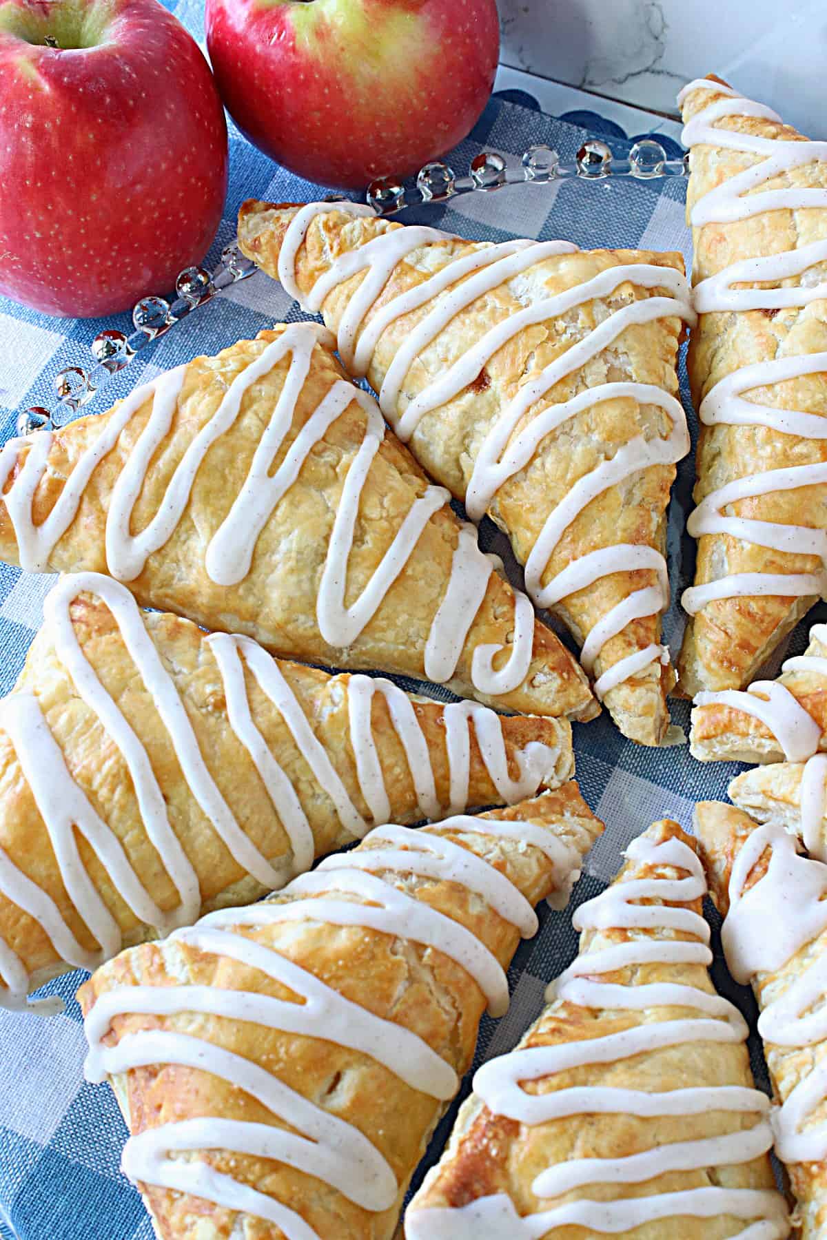 A glass platter filled with Puff Pastry Apple Turnovers with an icing drizzle.
