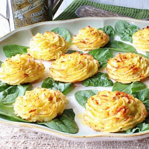 Pretty yellow duchess potatoes on a platter with spinach leaves.