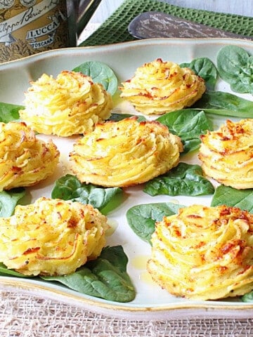 Pretty yellow duchess potatoes on a platter with spinach leaves.