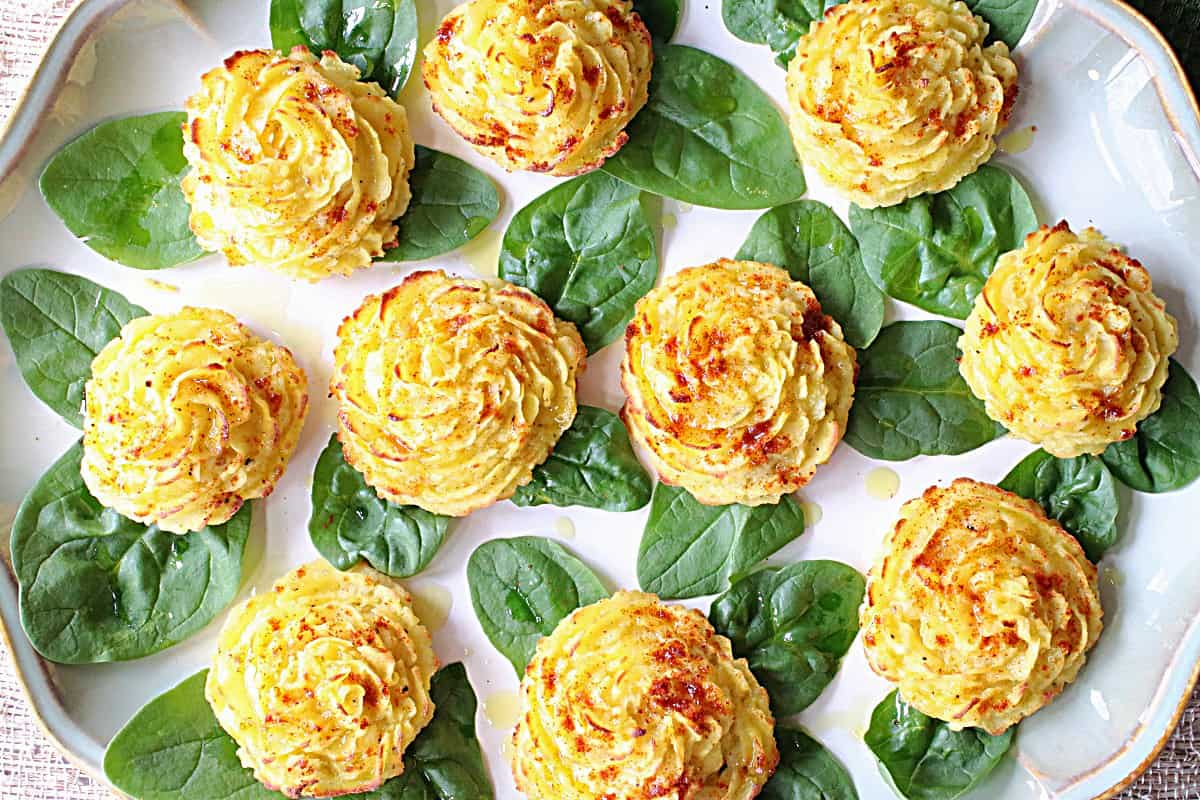 A bunch of pretty mashed potato rosettes on a platter with spinach leaves.