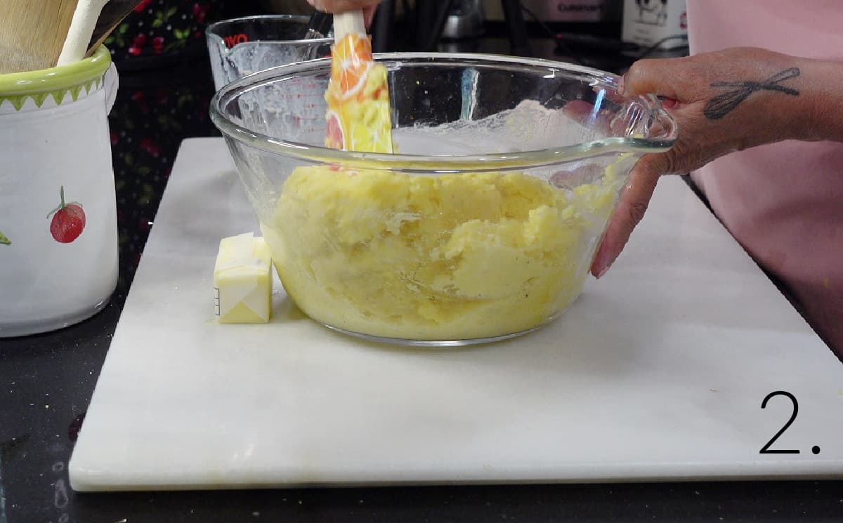 Mashed potatoes in a glass bowl with a spatula.