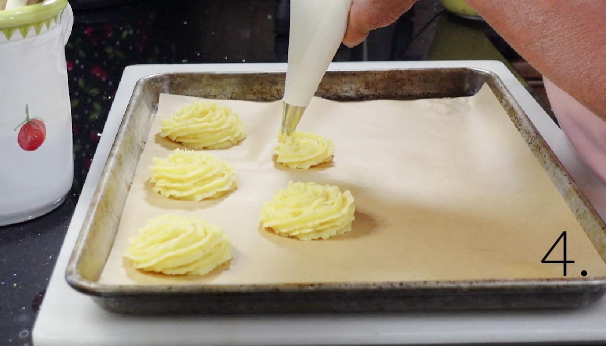 Duchess potatoes being piped out onto a baking sheet.