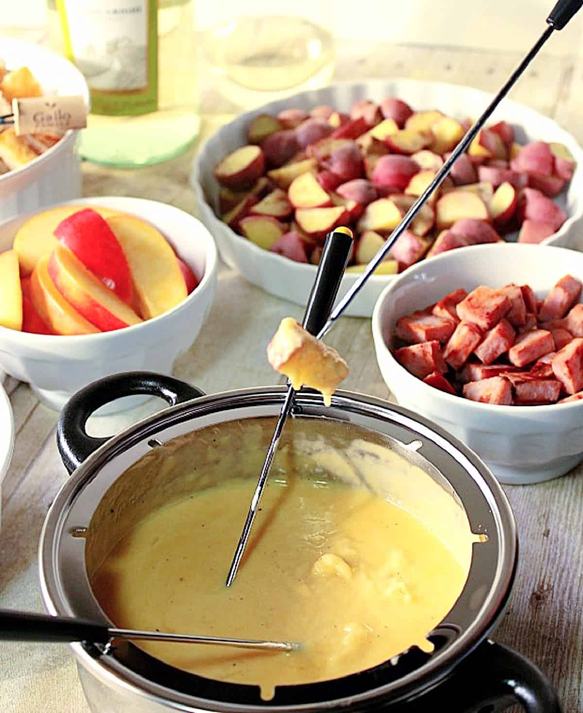 Fondue forks inside a fondue pot with cheese sauce dripping off a bread cube.